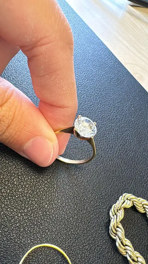 Kundenfoto: Solitärring aus Gold, zwischen zwei Fingern gehalten, daneben eine Kordelkette